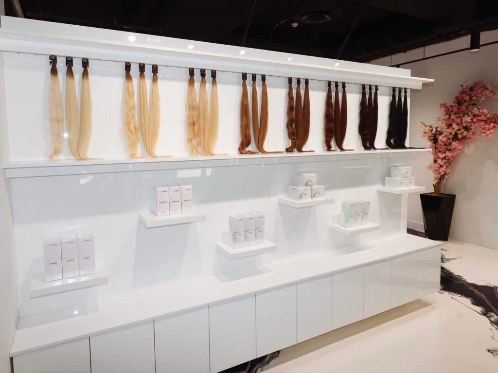 Extension hair in shades from platinum to espresso lined up on the wall at Neish Hair in Brickell