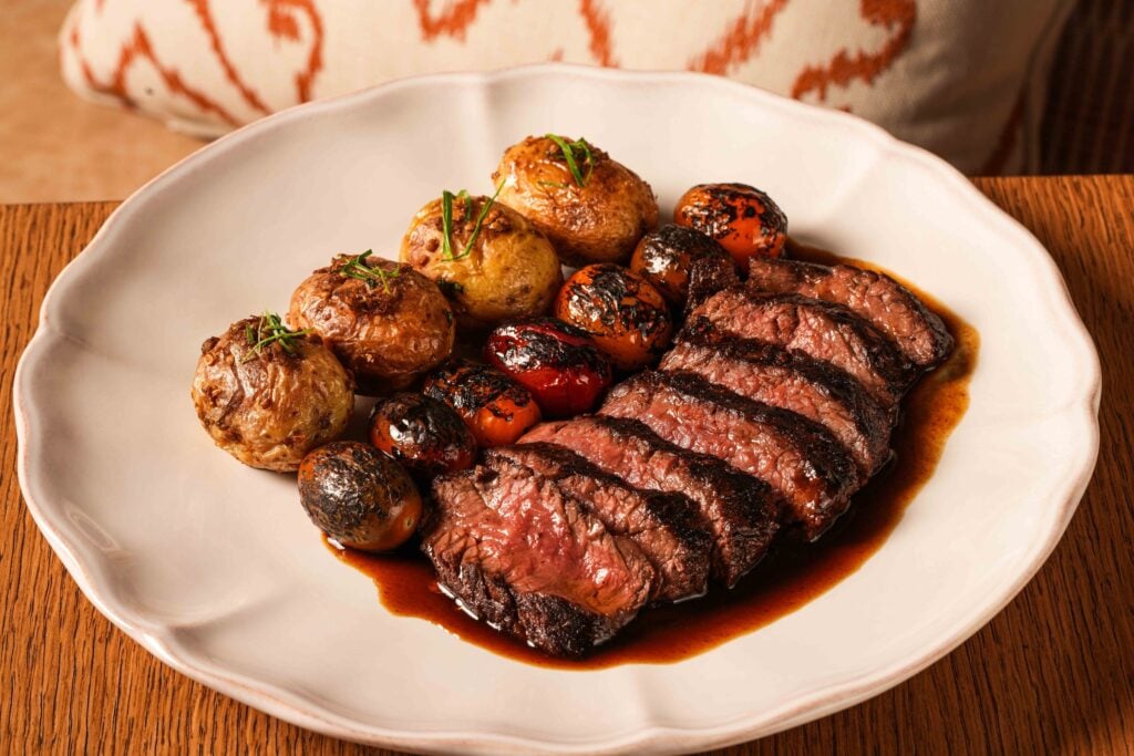 Sliced hanger steak at Aguasal by José Andrés, plated with cypriot potatoes and charred cherry tomatoes in a dark pan sauce.
