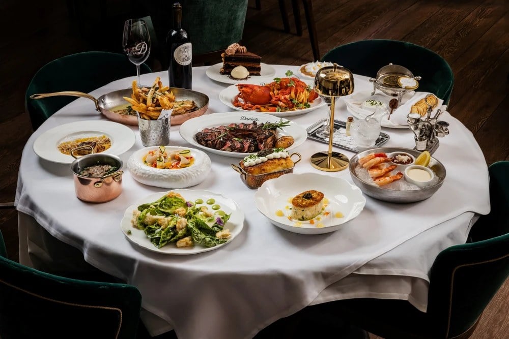 A full table spread at Daniel's Miami with a sliced steak, lobster pasta, shrimp cocktail, caviar service, caesar salad, fries, and a slice of chocolate cake.