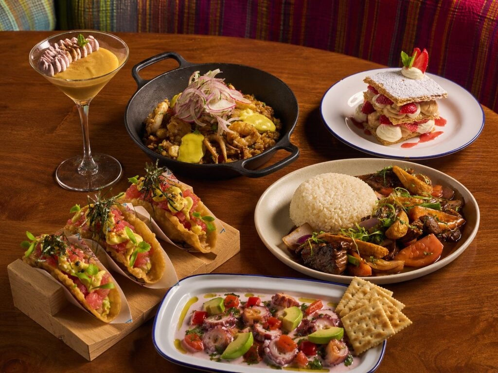 A spread of Peruvian dishes at Jarana Aventura, including wonton tacos, octopus ceviche, lomo saltado with rice, seafood rice, a pisco cocktail, and a strawberry millefeuille.
