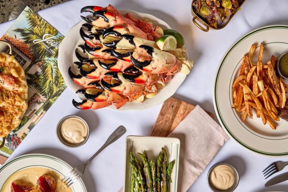 A platter of stone crab claws on ice at Joe's Stone Crab, served with mustard sauce, fries, grilled asparagus, and mac and cheese.