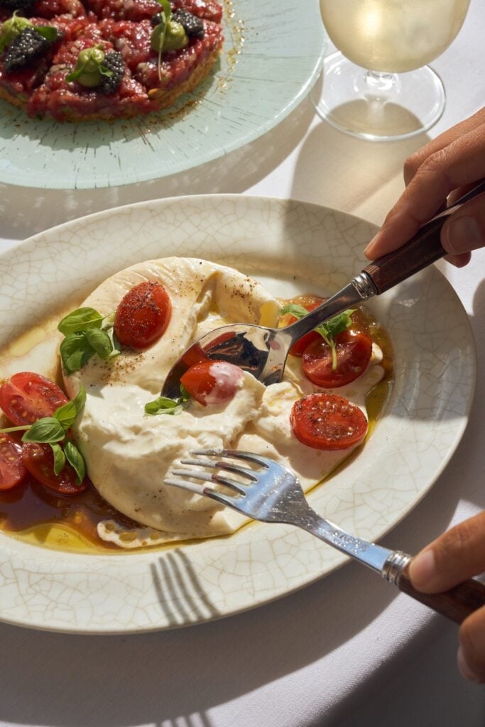 Burrata et tomates at LPM Restaurant & Bar, served with cherry tomatoes, basil, and olive oil alongside a beef tartare and a glass of white wine.