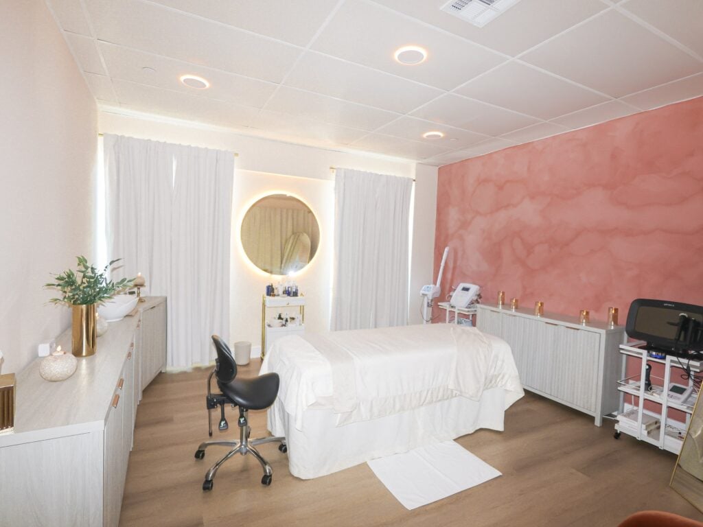 A treatment room at Skin House of Beauty with a draped facial bed and a rounded backlit mirror