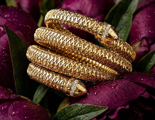 Coiled gold and diamond bracelets from Dover Jewelry & Diamonds arranged on dark red petals