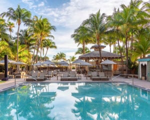 The palm-lined pool deck and thatched bar pavilion at The National Hotel Miami Beach