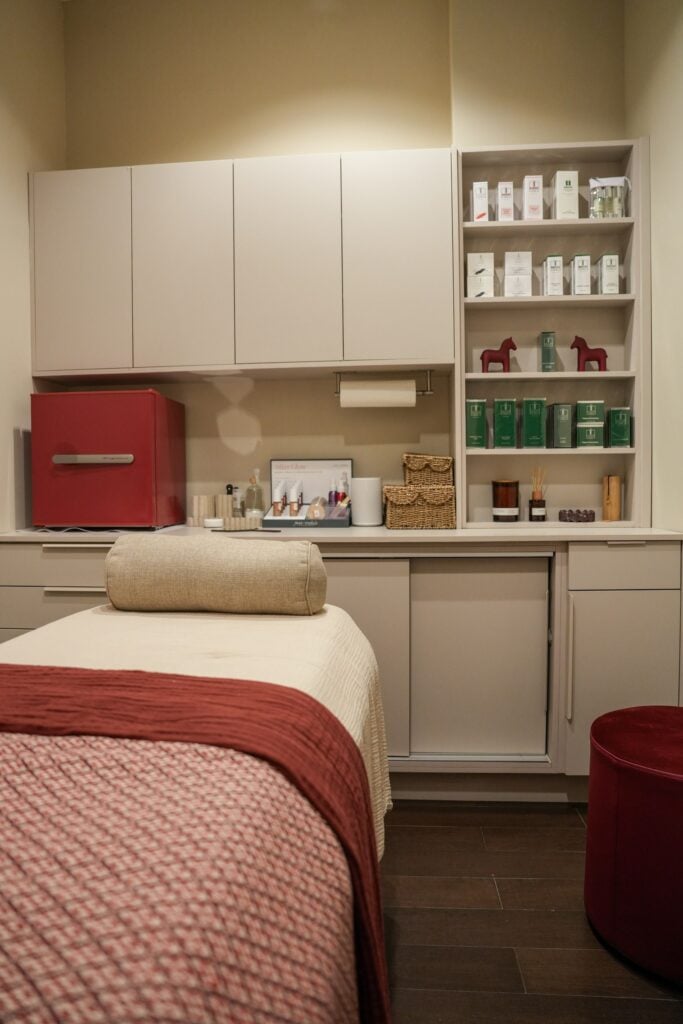 Shelves of skincare products above a treatment bed at Da Beauty Bar, with small red folk-art horses among the boxes