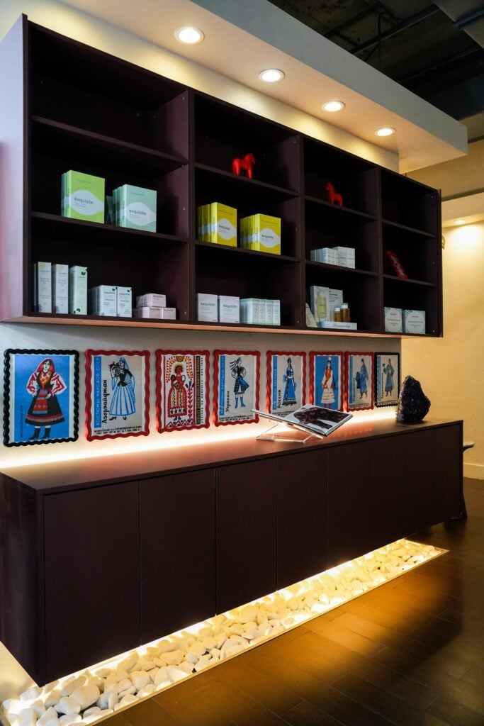 A retail wall at Da Beauty Bar lined with framed Russian folk-costume prints below shelves of skincare products