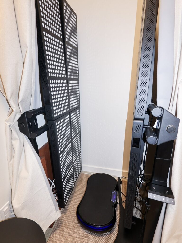 A red light therapy panel and vibration plate in a curtained bay at Evolve Longevity in Miami Beach