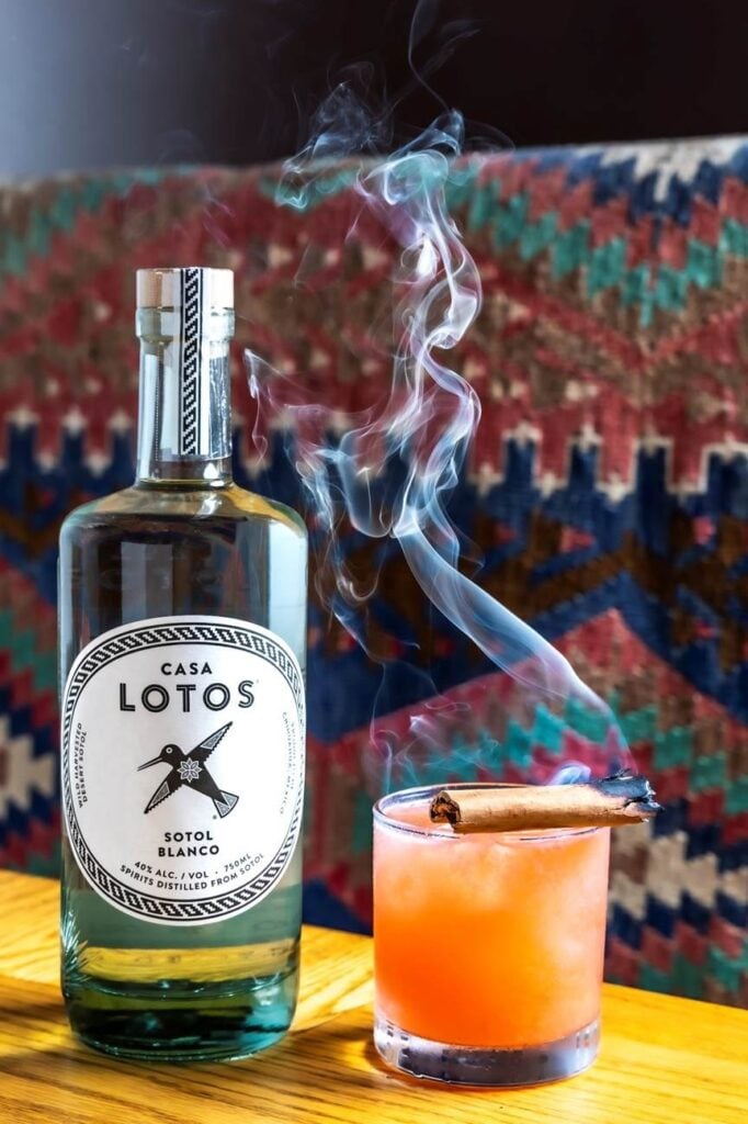 A bottle of Casa Lotos sotol blanco beside a strawberry sotol cocktail